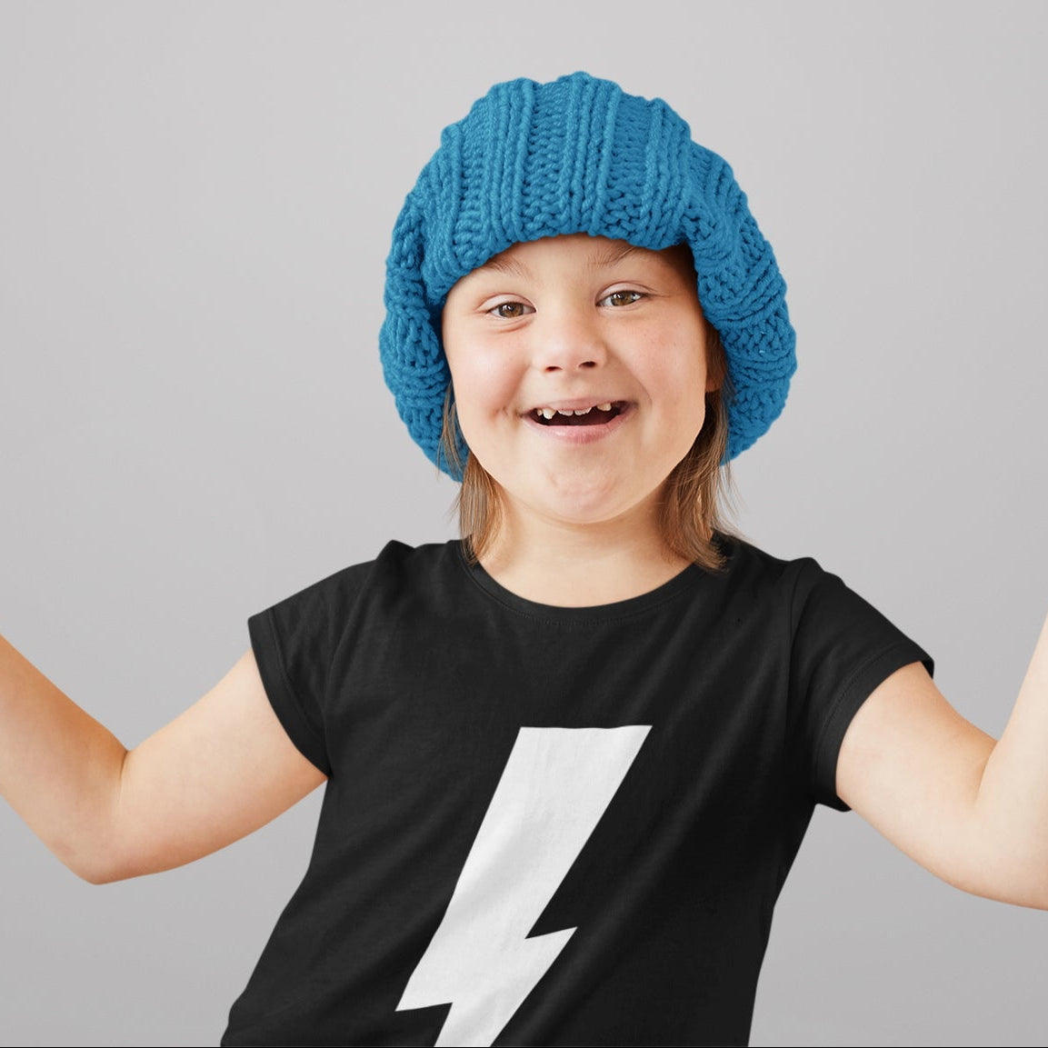 Child wearing a blue knit hat and black t-shirt with a white lightning bolt on a gray background