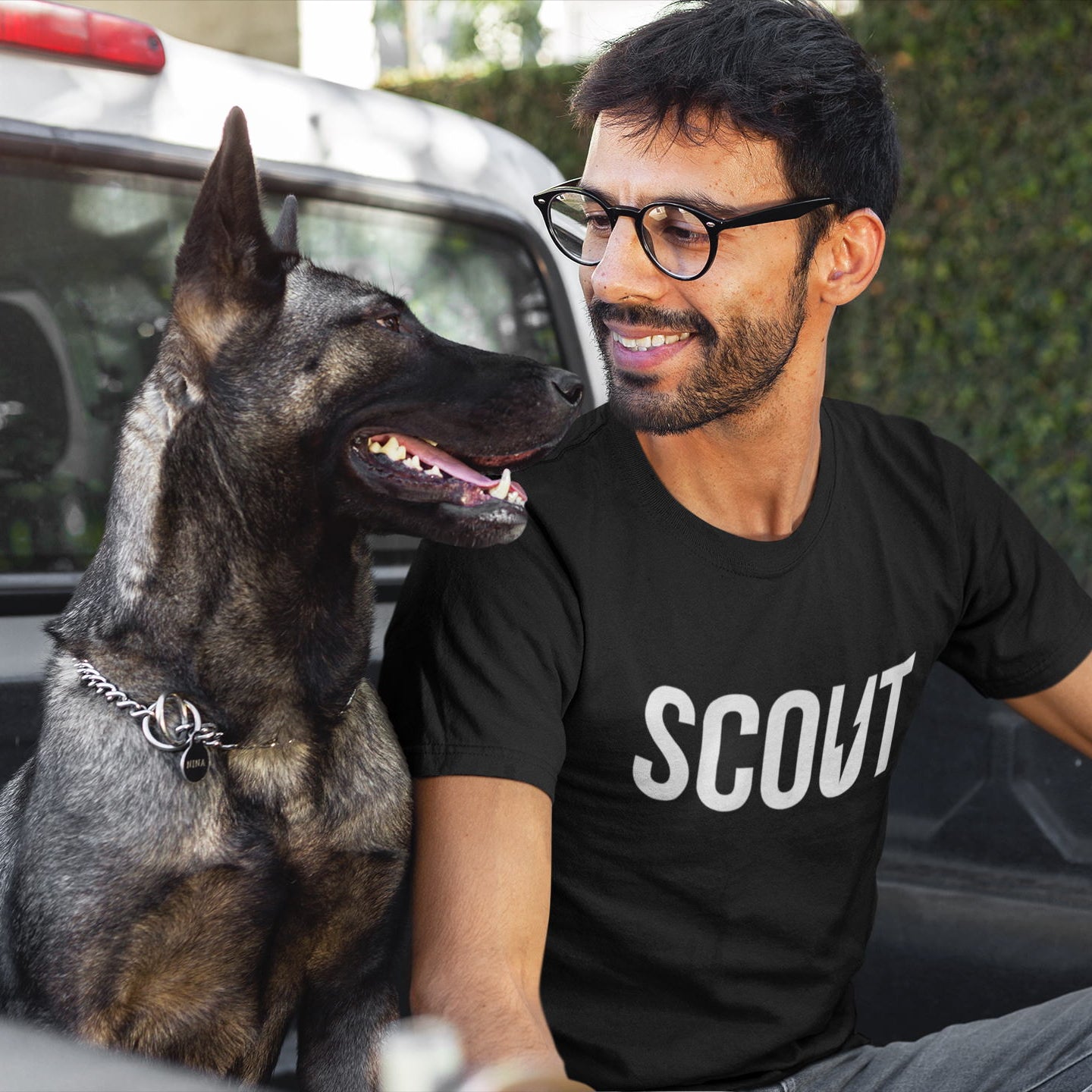 Man wearing a black 'SCOUT' t-shirt sitting next to a dog in a vehicle.